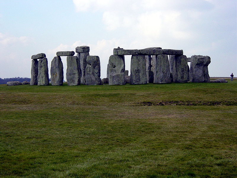 A collection of large stones in the middle of a field. The stones are set upright in a circle. Some flat stones lay on top of the others.